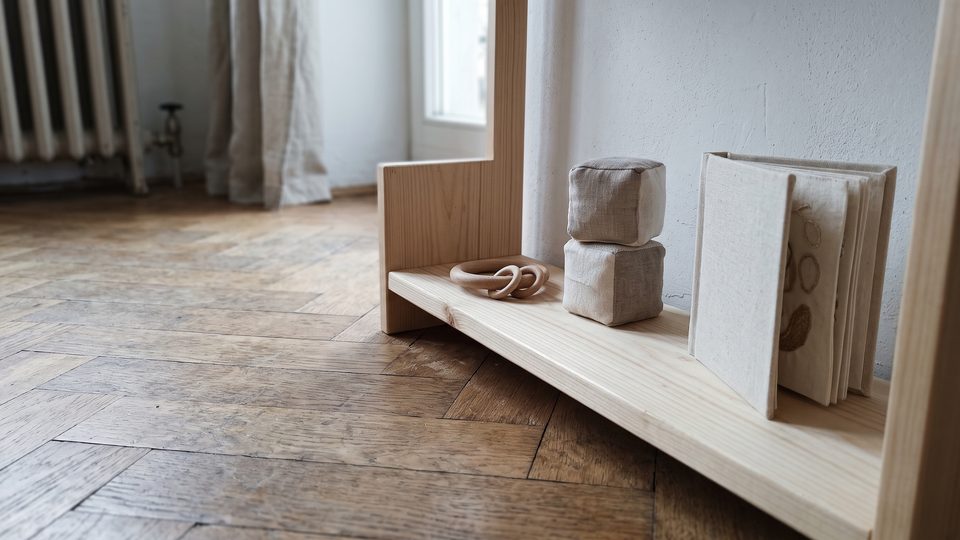 Étagère basse en bois sur un parquet, avec trois objets d'éveil posés à distance les uns des autres